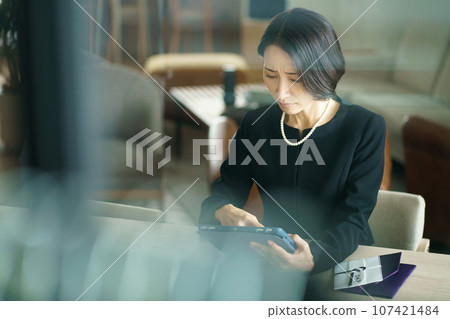 A woman in mourning clothes looking at a tablet device 107421484