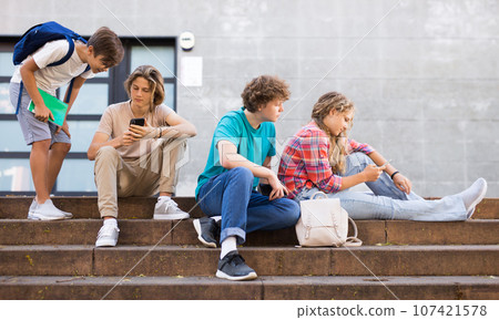 Teens with smartphones on stairs beside shool building 107421578