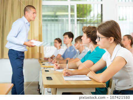 Teenage girl with glasses studying in college with classmates Teenage girl with glasses studying in college with classmates 107421580
