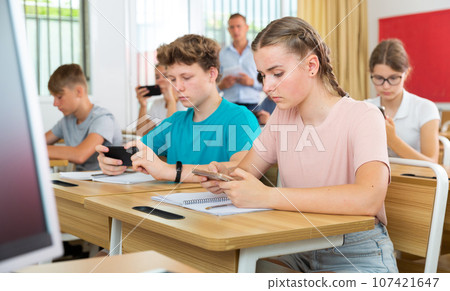 Teenager students sitting in class room with smartphones 107421647