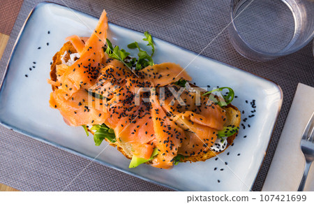 Delicious smoked salmon with arugula avocado and seeds on fried bread Delicious smoked salmon with arugula avocado and seeds on fried bread 107421699