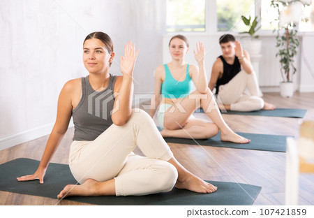 Group of young people doing a spinal twist pose. Group of young people doing a spinal twist pose. 107421859