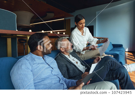 Focused business team working on project together while sitting on sofa in cozy coworking 107423945