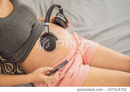 Melodies in the womb: Headphones placed on a pregnant belly, bonding through music, a heartwarming connection between mother and baby 107424782