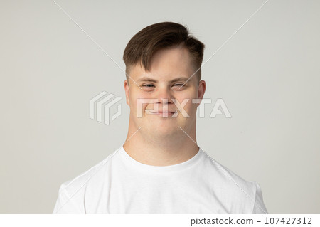 A smiling young man with cerebral palsy in glasses and a white T-shirt poses for the camera. World Genetic Diseases Day concept 107427312