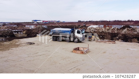 Truck laden with dirt and soil travels in a road construction complex site. Dump truck unloading soil or sand at construction site. 107428287