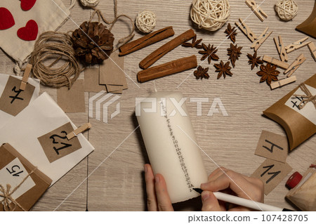 Unrecognizable young woman paint numbers on candles. Female making homemade advent calendar Made with your own hands step by step DIY crafts do it yourself. Preparation to christmas concept. Seasonal Unrecognizable young woman paint numbers on candles. Female making homemade advent calendar Made with your own hands step by step DIY crafts do it yourself. Preparation to christmas concept. Seasonal 107428705