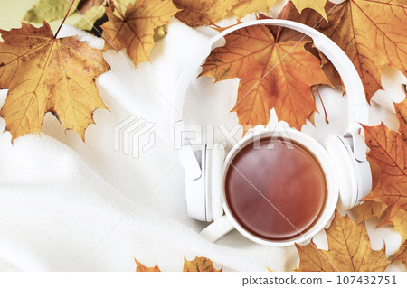 A Cup of hot coffee or tea with autumn leaves and headphones on a knitted white plaid background A Cup of hot coffee or tea with autumn leaves and headphones on a knitted white plaid background 107432751