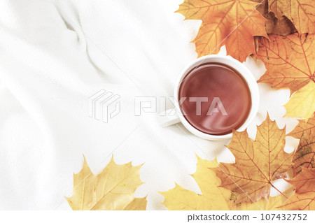 white cup of coffee or tea with golden autumn leaves on a knitted white plaid background .top view. white cup of coffee or tea with golden autumn leaves on a knitted white plaid background .top view. 107432752