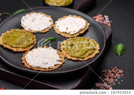 Round snacks with crispy chips or crackers with cream cheese and pesto 107433933