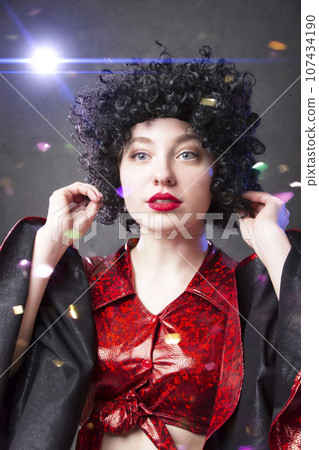 A beautiful disco girl in an African American wig against the background of flying confetti. Girl at a retro disco party. A beautiful disco girl in an African American wig against the background of flying confetti. Girl at a retro disco party. 107434190