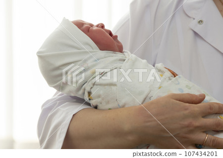 The doctor's hands hold a newborn baby wrapped in a diaper. 107434201