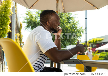 A young African-American man with a smartphone in his hands is sitting at a table 107434343