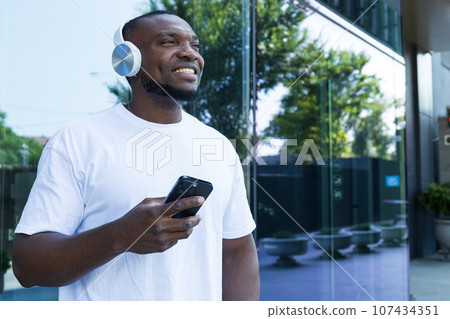 Stylish young African-American man listening to music in headphones with a smartphone in his hands 107434351