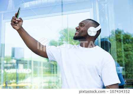 Stylish young African-American man listening to music in headphones with a smartphone in his hands Stylish young African-American man listening to music in headphones with a smartphone in his hands 107434352