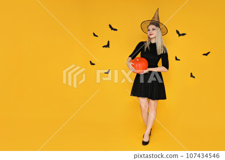 A girl in a Halloween costume with a pumpkin in her hands A girl in a Halloween costume with a pumpkin in her hands 107434546