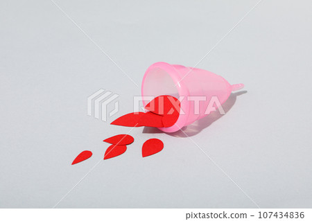 Pink menstrual cup with red drops in the middle, on a gray background Pink menstrual cup with red drops in the middle, on a gray background 107434836