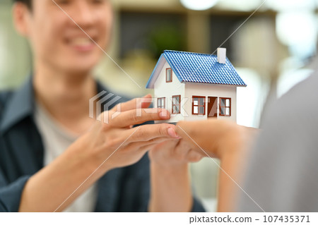 Closeup young couple hands holding a house model. Buying property, real estate, loan and insurance 107435371