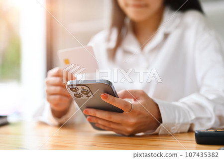 Happy young woman holding credit card and using smart phone, shopping on Internet or payment online Happy young woman holding credit card and using smart phone, shopping on Internet or payment online 107435382