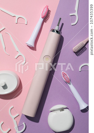 Electric toothbrush and dental floss on pink and purple background, top view 107435399