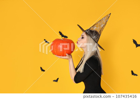 A girl in a wizard's hat kisses a pumpkin, on a yellow background A girl in a wizard's hat kisses a pumpkin, on a yellow background 107435416