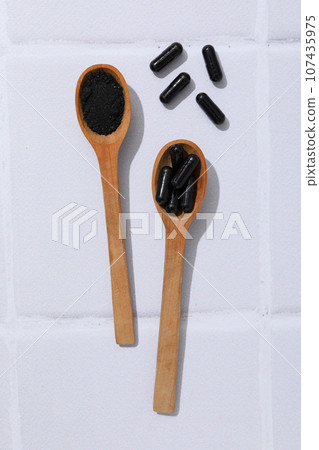 Activated charcoal tablets with wooden spoons on a light background 107435975
