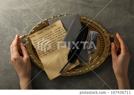 Vintage letter with text, envelope and feather on golden tray in hands, gray background, top view 107436711