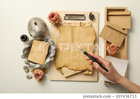 Vintage paper on wooden folder, silver box, roses and pen in hand on white background, top view 107436713