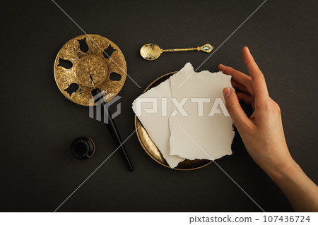 Papers, female hand, golden plates and spoon, ink bottle and pen on dark gray background, top view Papers, female hand, golden plates and spoon, ink bottle and pen on dark gray background, top view 107436724