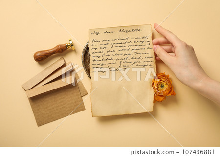 Vintage letter with text, hand, envelopes, rose and stamp on beige background, top view Vintage letter with text, hand, envelopes, rose and stamp on beige background, top view 107436881