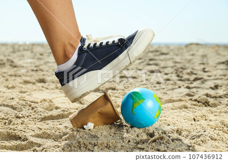 A leg with trash and a globe on the sand A leg with trash and a globe on the sand 107436912