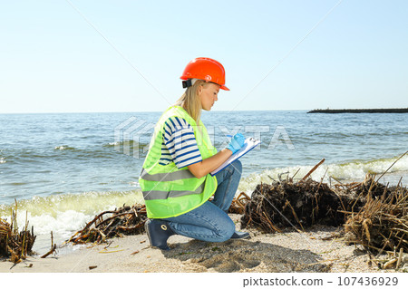 A woman in a helmet and overalls examines the pollution of the river A woman in a helmet and overalls examines the pollution of the river 107436929