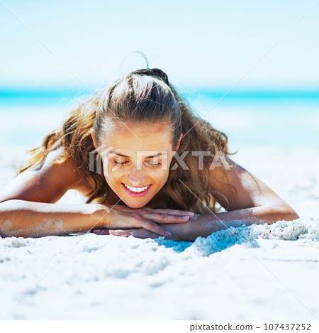 Happy young woman in swimsuit laying on beach Happy young woman in swimsuit laying on beach 107437252