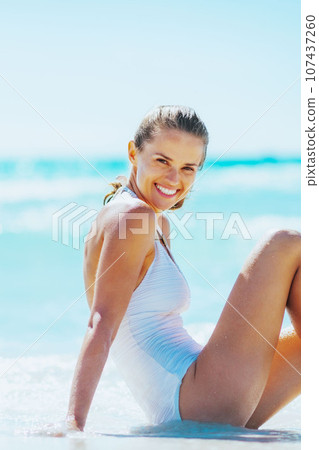 Smiling young woman sitting at seaside 107437260