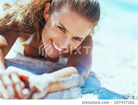 Happy young woman in swimsuit relaxing on beach Happy young woman in swimsuit relaxing on beach 107437262