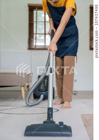 Asian woman cleaning in living room at home. Housekeeper or maid cleaner feel happy use vacuum cleaner to clean 107437498