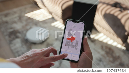 Woman presses the button on the app to turn on the modern robot vacuum cleaner. Modern technology of smart cleaning. Woman presses the button on the app to turn on the modern robot vacuum cleaner. Modern technology of smart cleaning. 107437684