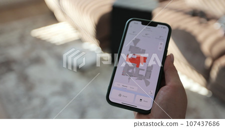 Woman using robot vacuum cleaner app on smartphone, white robot vacuum cleaner performs automatic cleaning of the apartment. Woman using robot vacuum cleaner app on smartphone, white robot vacuum cleaner performs automatic cleaning of the apartment. 107437686