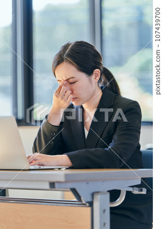 A young woman puts her hand between her eyebrows while operating a computer A young woman puts her hand between her eyebrows while operating a computer 107439700