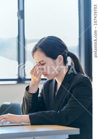A young woman puts her hand between her eyebrows while operating a computer A young woman puts her hand between her eyebrows while operating a computer 107439703