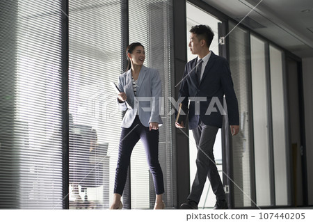 two asian business people on their way to meeting talking while walking in office two asian business people on their way to meeting talking while walking in office 107440205