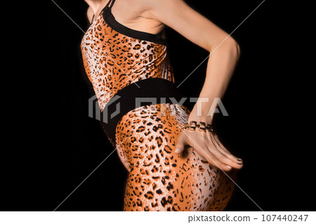 Thin young girl in leopard pattern suit posing and seducing, attracting attention with her hand on a black background Thin young girl in leopard pattern suit posing and seducing, attracting attention with her hand on a black background 107440247