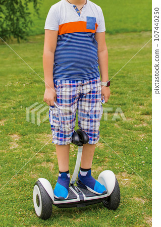 A boy portrait in a T-shirt and sneakers, stands on a hoverboard in a park on the street A boy portrait in a T-shirt and sneakers, stands on a hoverboard in a park on the street 107440250