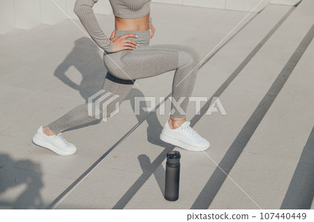Slender woman in gray sportswear doing exercises outdoors on stair, forward lunges 107440449