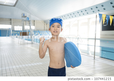 A boy doing a fist pump while holding a beat board in an indoor pool 107441215