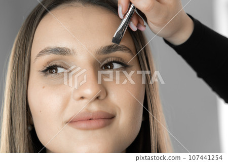 The photo captures the moment when the makeup artist works on every detail, creating eyebrows that emphasize individuality and natural beauty face beautifully woman in beauty salon. Work cosmetologist 107441254