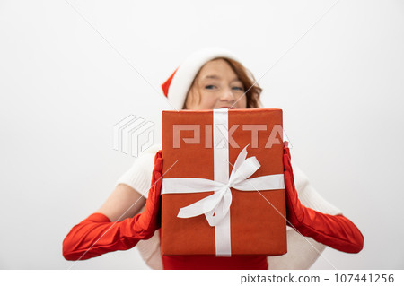 Smiling slightly, she holds a gift in her hands, which will become an expression of love and care for loved ones for the New Year and Christmas. Against the background of a white sheet of paper, the 107441256