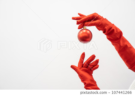 The hands of woman in elegant red dress and gloves hold bright Christmas ball, ready to add shine to any Christmas composition. Winter holidays and atmosphere new year and preparations for Christmas. The hands of woman in elegant red dress and gloves hold bright Christmas ball, ready to add shine to any Christmas composition. Winter holidays and atmosphere new year and preparations for Christmas. 107441266