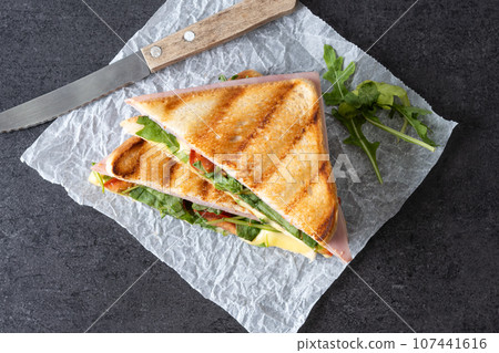 Panini sandwich with ham, cheese, tomato and arugula on black slate background 107441616