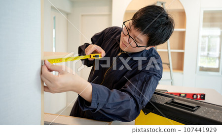 Asian male furniture assembler using tape measure Asian male furniture assembler using tape measure 107441929